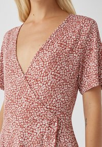 Vestido cruzado en color óxido, con un pequeño patrón floral en blanco. Tejido suave con mangas cortas y escote en V. Detalle de cintura anudada.