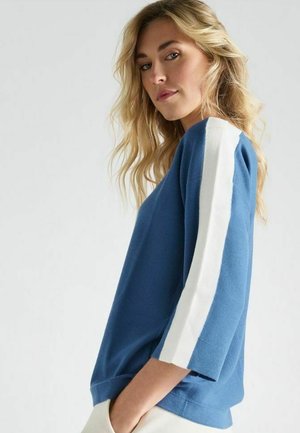 Blauwe sweatshirt met witte gestreepte accenten op de mouwen. Zachte textuur, ontspannen pasvorm en driekwartmouwen. Subtiel modern ontwerp.