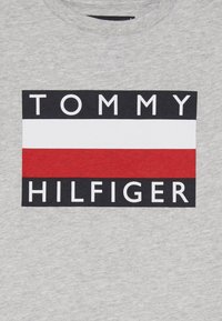 Graues Baumwoll-T-Shirt mit einem schwarzen rechteckigen Logo und weißen Buchstaben "TOMMY HILFIGER" sowie einem horizontalen rot-weißen Streifenmuster.