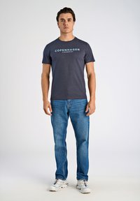 Mörkblå bomulls t-shirt med "KÖPENHAMN" tryckt i ljusblå, matchad med medelvattens tvättade jeans och vita sneakers.