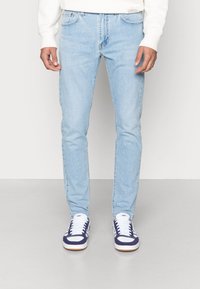 Ljust blå denimjeans med slim fit, som har framfickor, en klassisk femfickedesign och subtila blekningar. Matchas med vita och marinblå sneakers.
