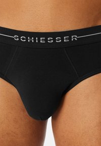 Svarta bomullsboxershorts med ett mjukt, elastiskt midjeband som har varumärket "SCHIESSER" i grått. Slät textur, åtsittande design.
