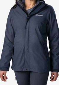 Marinblå vattentät jacka från Berghaus med dragkedja fram, justerbara manschetter och en hög krage med huva. Mjuk, texturerad tyg.