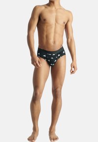 Mustat alushousut, joissa on valkoinen kolmiomallinen logokuosi, elastinen vyötärönauha, puuvillamateriaali, istuva muotoilu ja minimaalinen peitto.