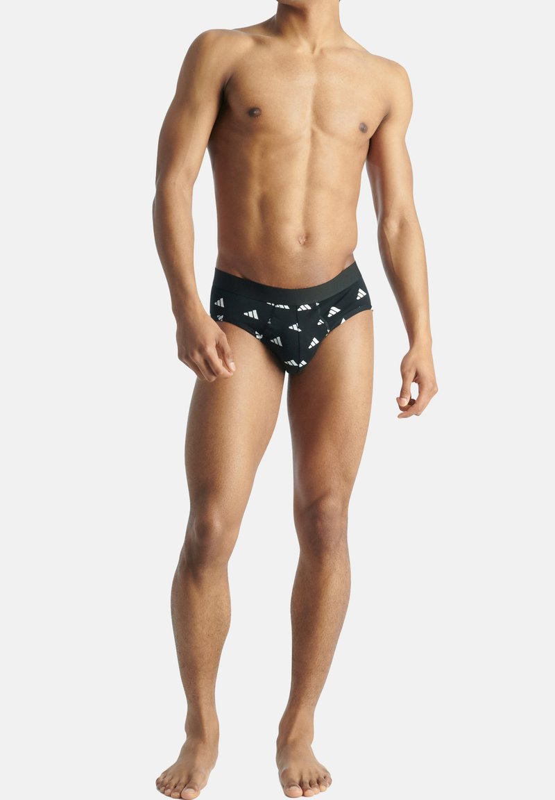 Mustat alushousut, joissa on valkoinen kolmiomallinen logokuosi, elastinen vyötärönauha, puuvillamateriaali, istuva muotoilu ja minimaalinen peitto.