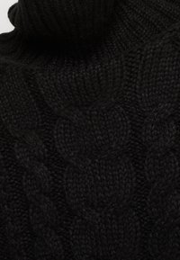 Schwarzer Strickpullover mit Zopfmuster und hohem Kragen. Die Textur ist dick und zeigt sichtbare Fasern, die Wärme und Stabilität bieten.