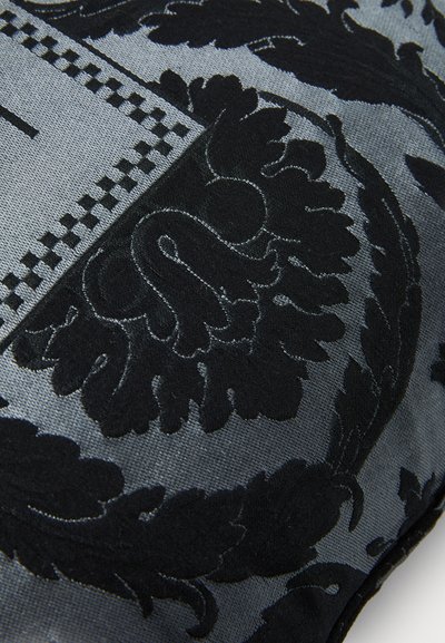 Melna un pelēka spilvena ar sarežģītu ziedu rakstu, kurā redzama teksturēta izšuvuma un gludas fona kombinācija. Kvadrāta forma ar šūtiem malām.