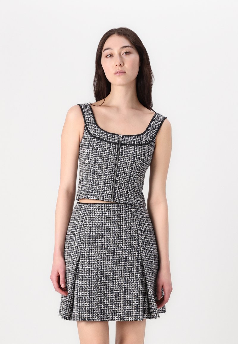 Ensemble en tweed noir et blanc composé d'un haut zippé court et d'une jupe évasée, avec un tissu texturé et des finitions contrastées.