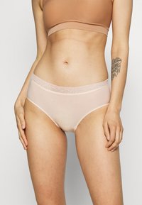 Culotte taille haute beige clair avec une ceinture accentuée de dentelle, en tissu lisse et avec un design sans couture pour le confort et l'ajustement.