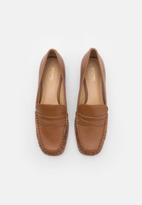 Mocassins en cuir marron à finition lisse, avec des coutures détaillées autour des bords et un accent subtil sur l\'orteil. Logo visible sur la semelle intérieure.
