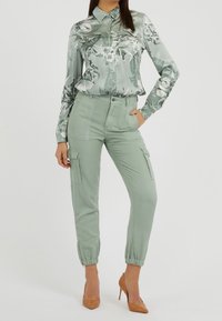 Langärmlige Bluse mit Blumenmuster in Hellgrün, kombiniert mit hellgrünen Cargo-Hosen mit Bündchen und Taschen; getragen mit hellbraunen High Heels.