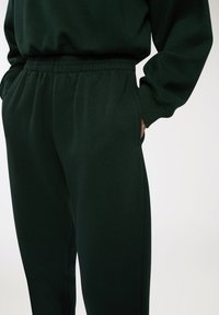 Ciemnozielone dresy o luźnym kroju, z elastycznym paskiem w talii i bocznymi kieszeniami, wykonane z miękkiej, fakturowanej tkaniny.