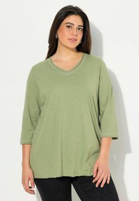 Zelený, lehký, dlouhý rukáv top s výstřihem do V, se subtilními detaily šití. Volný střih se pohodlně přizpůsobuje tělu.