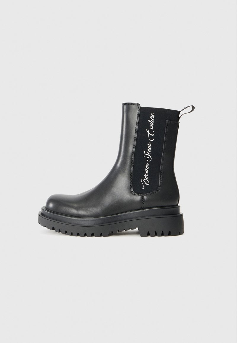 Botas de tornozelo em couro preto com sola chunky, apresentando painéis laterais elásticos e texto de logotipo branco de um lado.