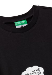 Černé bavlněné tričko s kulatým výstřihem, na kterém je bílá grafika ve tvaru mraku s textem. Nálepka říká "UNITED COLORS OF BENETTON."