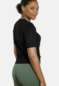 Black short-sleeve top in a fitted design, made from a soft material. Paired with green high-waisted pants, emphasizing a sleek silhouette.