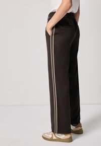 Pantaloni larghi neri con una texture morbida, dotati di due strisce laterali beige a contrasto, vita elastica e tasche laterali.