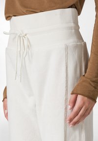 Weiße Textilhosen mit einem breiten, strukturierten Bund und Kordelzug, ausgestattet mit Seitentaschen und kontrastierenden Nähten für zusätzlichen Detailreichtum.