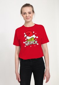 Červené tričko s potiskem pohádkového Grinche v santovské čepici, s textem "GRINCH" v zelené barvě a bílými hvězdami kolem designu. Bavlněný materiál.
