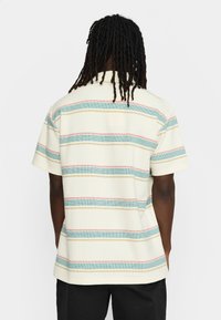 Korte mouwen polo shirt in roomkleur met horizontale strepen in aqua, rood en geel. Gearchiteerd stof met een relaxte pasvorm en kraag.