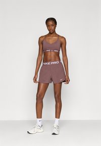 Αθλητικό σουτιέν και σορτς Nike Pro σε βαθύ μοβ χρώμα. Τα σορτς διαθέτουν λευκή ζώνη μέσης με το λογότυπο Nike Pro, ενώ το σουτιέν έχει αντίστοιχη ζώνη.