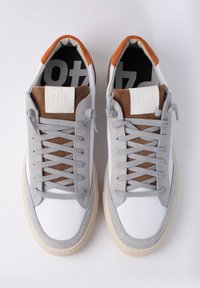 Zapatillas de ante gris y cuero blanco con acentos marrones, cordones planos grises, punta redonda y suela de goma crema. Logo de la marca en la lengüeta.