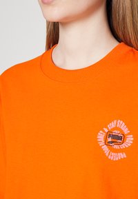 Helderoranje katoenen t-shirt met een ronde hals en korte mouwen, voorzien van een wit grafisch ontwerp op de borst.