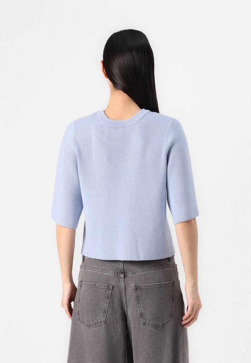 Jasnoniebieski, prążkowany sweter z krótkim rękawem i okrągłym dekoltem, zestawiony z ciemnoszarymi spodniami o szerokich nogawkach, widoczny z tyłu.