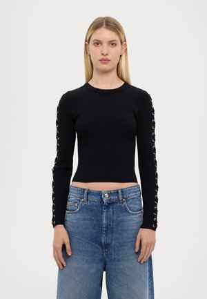 Zwarte geribbelde lange mouwen top met gouden eyelets langs de mouwen, gecombineerd met hoge taille blauwe denim jeans.