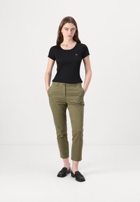 Juodas trumpas rankovėmis marškinėliai su sagų detalėmis, derinami su alyvuogių žalumo siaurėjančiais džinsais. Modelis vilki juodus loafers batus, minimalistinio dizaino, lygia tekstūra.