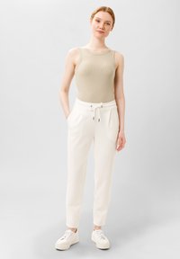 Top in cotone a coste di un beige chiaro abbinato a pantaloni jogger bianchi a gamba affusolata con vita elastica e lacci, indossato con sneakers bianche.