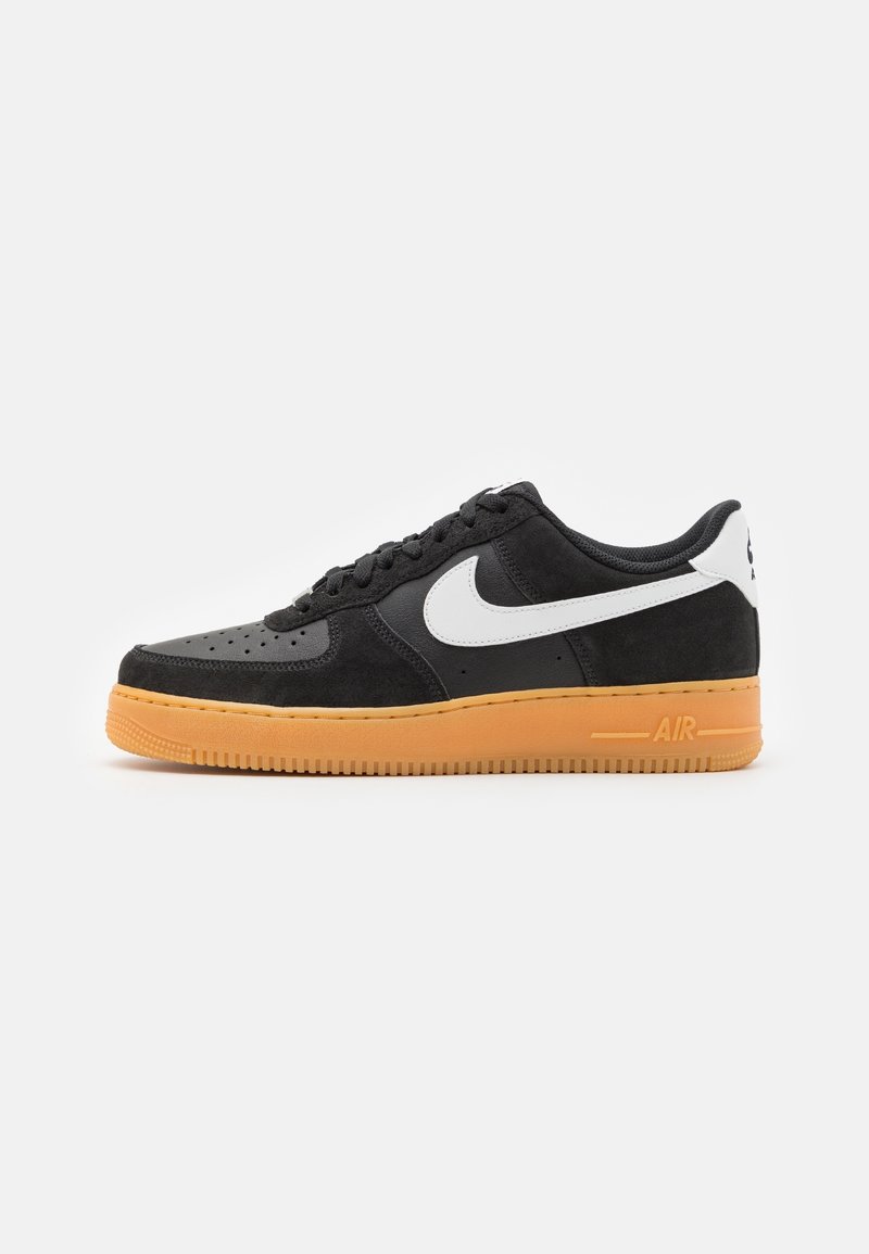 Baskets Nike Air Force 1 noires avec logo swoosh blanc et languette au talon, avec une semelle en caoutchouc naturel, présentées sur un fond blanc uni.