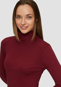 Burgunderfarbener Rollkragenpullover aus einem weichen, dehnbaren Stoff, mit langen Ärmeln und taillierter Silhouette. Glatte Textur, minimale Details.