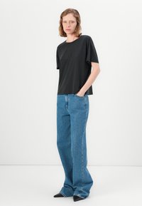 Svart kortermet t-skjorte med avslappet passform, sammen med lyseblå høytlivs vid jeans og svarte spisse sko.