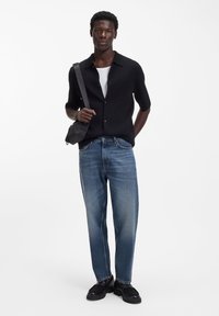 Cămașă neagră cu nasturi și mâneci scurte peste un maiou alb, asortată cu blugi drepti, de culoare albastru deschis, și pantofi negri. Ține o geantă mică neagră.