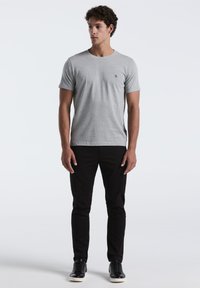 Grijze katoenen t-shirt met een ronde hals en korte mouwen, gecombineerd met zwarte slim-fit broek en zwarte sneakers met witte zolen.