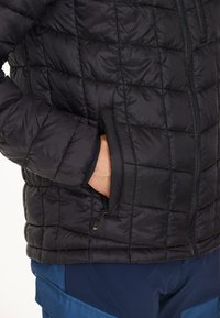 Sort quiltet pufferjakke med lynlås foran, sidelommer og tekstureret stof. Har en slank pasform og let isolering.