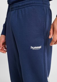 Granatowe dresowe spodnie sportowe z rypsowym pasem, z białym logo i tekstem na lewej udzie. Wykonane z miękkiego, oddychającego materiału.