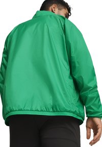 Veste légère verte avec une texture lisse, ourlet élastique et col. Présente un design épuré sans fermetures visibles.