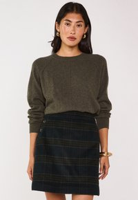 Maglione lavorato a maglia verde oliva con maniche raglan; gonna mini in plaid di lana in blu navy scuro e verde con bottoni decorativi sul lato.