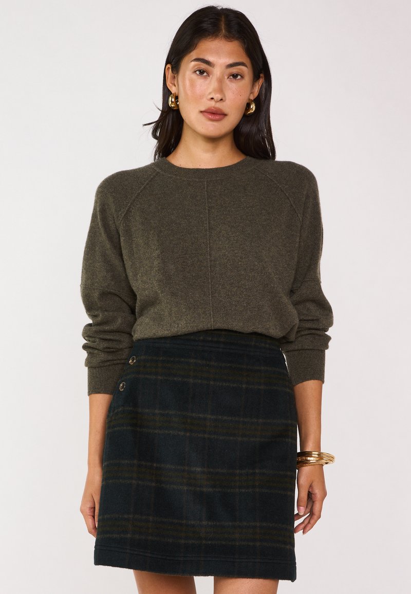 Maglione lavorato a maglia verde oliva con maniche raglan; gonna mini in plaid di lana in blu navy scuro e verde con bottoni decorativi sul lato.