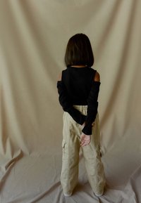 Zwarte lange mouwen top met open schouders, gecombineerd met lichtbeige cargobroek met zakken, gezien vanuit de achterkant tegen een neutrale achtergrond.