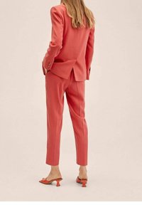 Coral suit with tailored blazer and tapered pants. Textured fabric. Notable double vents on blazer. Pointed heeled mules in matching color.