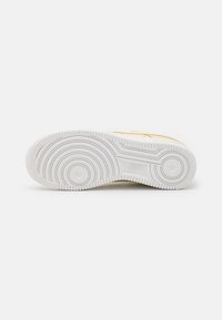 Nike sneaker outsole, white rubber, circular tread pattern with textured grip. Smooth edges and distinct branding detail near the heel.