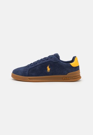 Marineblå ruskindssneakers med brun sål, gul logo på siden og gul hælmarkering, mærket med Polo-tekst på sålen.
