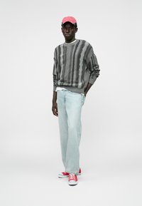 Γκρίζος πλεκτός πουλόβερ με σχέδια, ανοιχτό μπλε παντελόνι σε φαρδιά γραμμή και κόκκινα αθλητικά παπούτσια. Περιλαμβάνει επίσης ένα ροζ καπέλο, αναδεικνύοντας ένα χαλαρό στυλ streetwear.