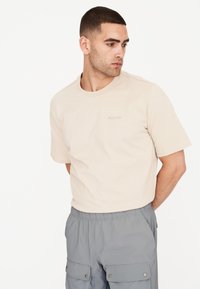 Beige puuvillane t-särk lühikeste varrukatega ja ümara kaelusega, mille esiküljel on peen brändi logo. Sobib hallide kargo lühikestega.