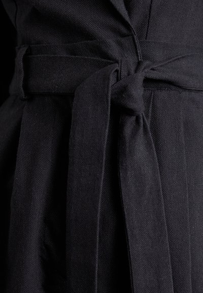 Rochie din țesătură neagră cu un finisaj texturat, având un cordon la talie. Imaginea de aproape arată cusături detaliate și un design ferm, bine structurat.