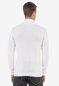 Pull polo blanc à manches longues avec un col et des poignets côtelés. Coupe ajustée, tissu tricot léger avec une texture lisse. Vue arrière présentée.