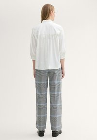 Witte shirt met een geraffineerde rug en driekwartmouwen, gecombineerd met geruite broek in grijze, zwarte en blauwe tinten, afgewerkt met zijsplitten.